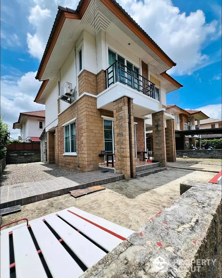 Charming two-story house with brick accents and a spacious yard under a clear blue sky.