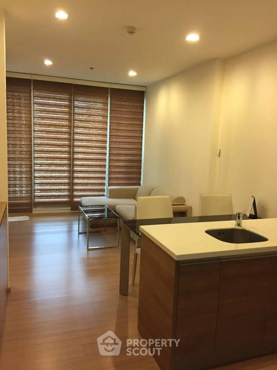 Modern living room with wooden flooring and large windows with blinds, featuring a cozy sofa and dining area.