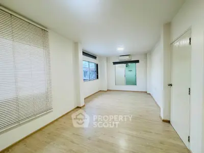 Spacious empty room with wooden flooring and large windows, perfect for customization.