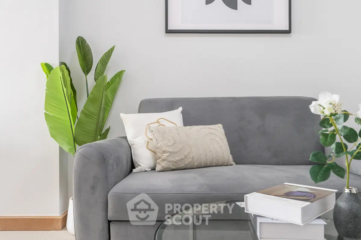 Modern living room with stylish gray sofa, decorative pillows, and lush green plant for a cozy ambiance.