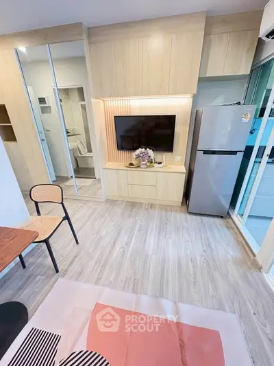 Modern living room with sleek wooden paneling, wall-mounted TV, and stainless steel fridge in a cozy apartment.