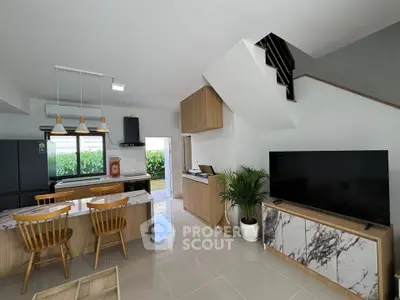 Modern open-plan living room with stylish kitchen and staircase, featuring sleek furniture and natural light.