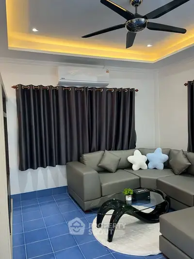 Modern living room with stylish gray sofa, blue floor tiles, and ceiling fan.
