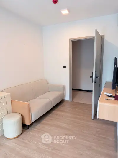 Modern living room with beige sofa and open door, showcasing minimalist design and wooden flooring.