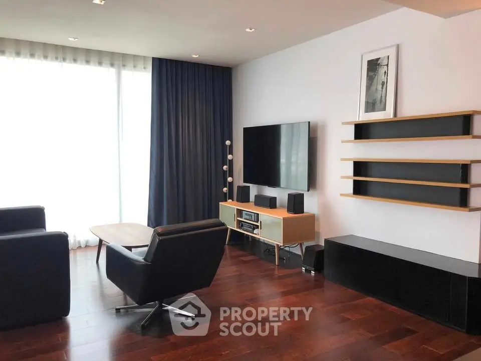 Modern living room with sleek furniture and large TV, featuring dark wood flooring and elegant curtains.