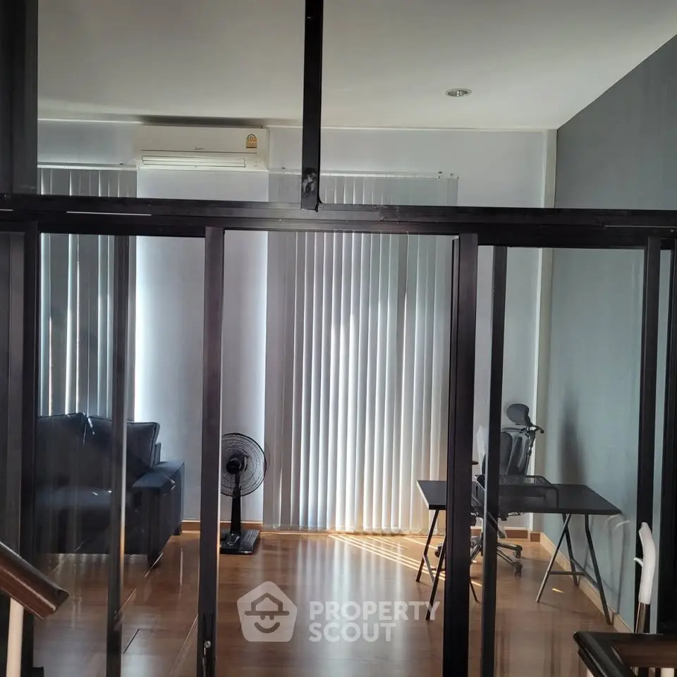 Modern living room with glass partition, sleek furniture, and natural light.