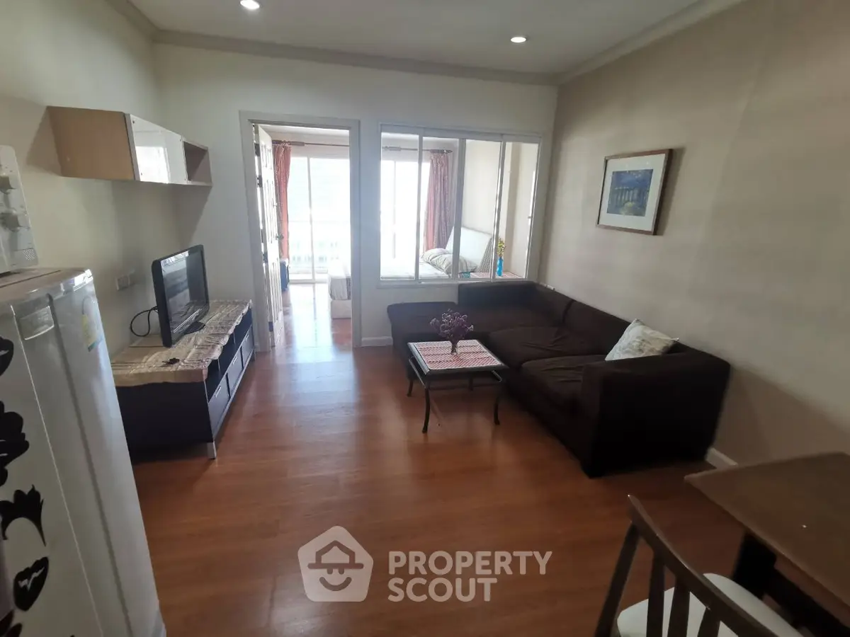 Cozy living room with wooden flooring and modern furniture, leading to a bright balcony with city views.