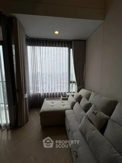 Cozy living room with plush sofa and panoramic city view through large windows.