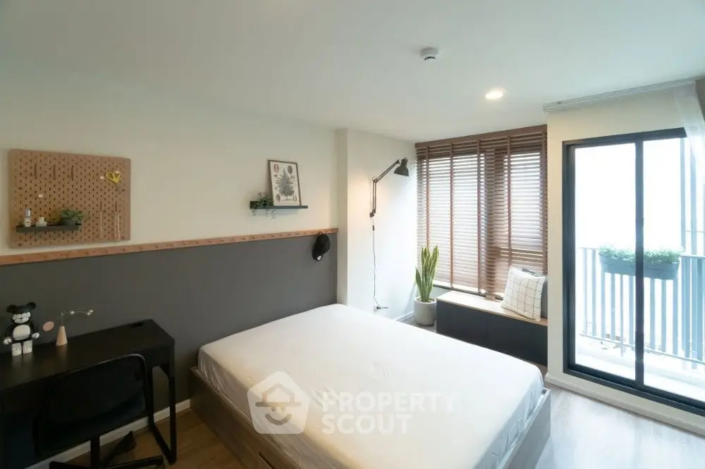Modern bedroom with large window and balcony access, featuring stylish decor and ample natural light.