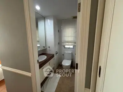 Modern bathroom with sleek design, featuring a large mirror, white cabinetry, and a compact toilet.