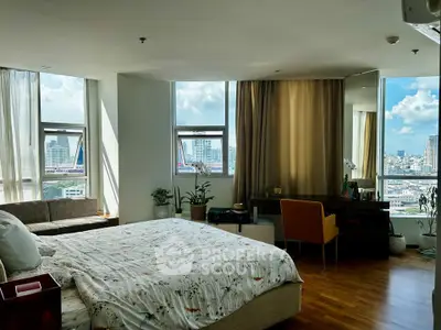 Spacious bedroom with city view, featuring cozy seating area and elegant decor.