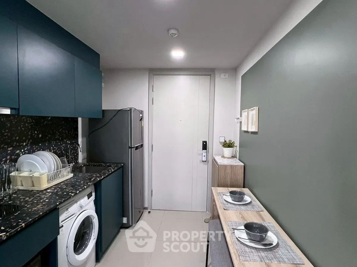 Modern kitchen with sleek cabinets, washing machine, and dining setup in compact space.