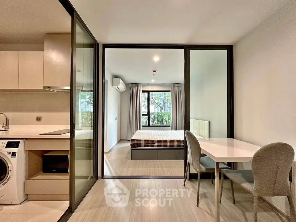 Modern studio apartment with open layout, featuring a cozy bedroom and compact kitchen with washing machine.