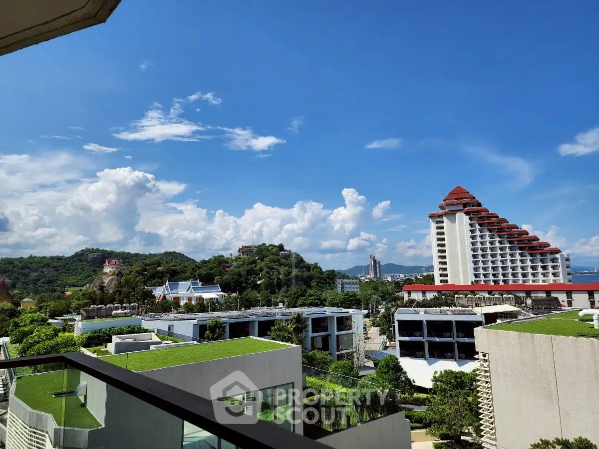 Stunning view from balcony overlooking lush green hills and modern architecture.