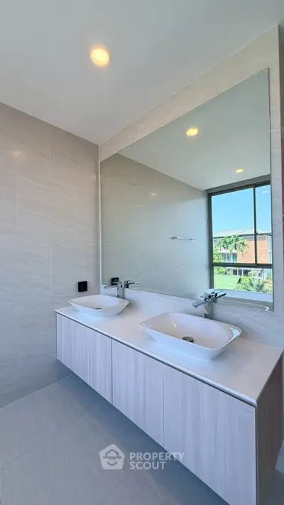 Modern bathroom with dual sinks and large mirror, featuring sleek design and natural light.