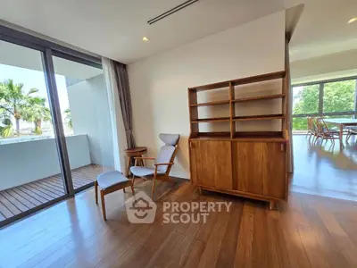 Spacious living room with wooden flooring and modern furniture, featuring a large balcony with lush views.