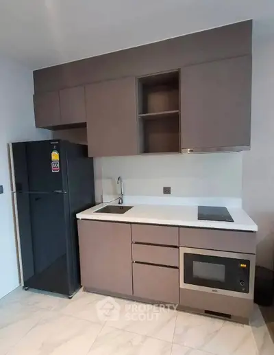Modern kitchen with sleek cabinetry, built-in microwave, and compact fridge in stylish apartment.