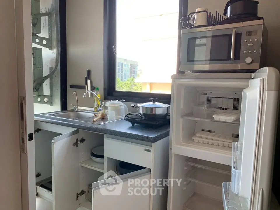 Compact kitchen with open cabinets, microwave, and mini fridge in modern apartment.