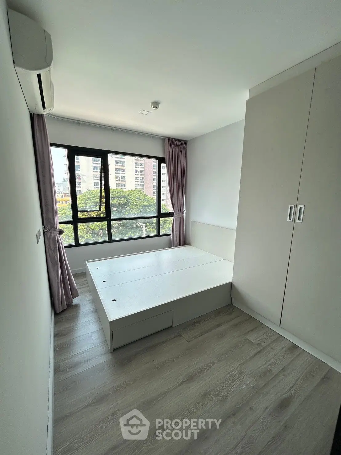 Modern bedroom with large window and built-in wardrobe, offering a serene view of the cityscape.