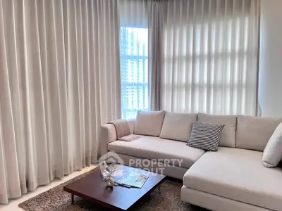 Elegant living room with a large sectional sofa, sheer curtains, and natural light streaming through the window, perfect for relaxation and entertaining guests.