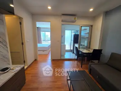 Modern apartment interior with open living area, kitchen, and bedroom view, featuring sleek furniture and wooden flooring.