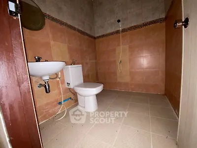 Spacious bathroom with tiled walls and floor, featuring a toilet and sink, ideal for modern living.