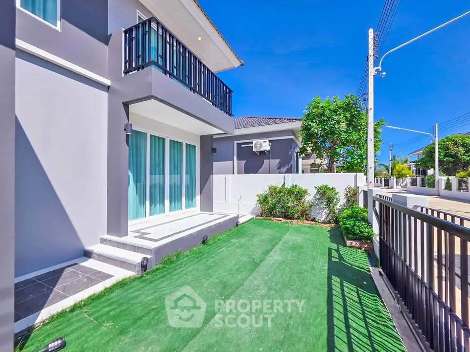 Modern two-story house with balcony and landscaped garden in a sunny neighborhood.