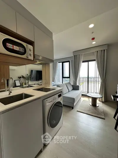 Modern open-layout living room with kitchen, featuring sleek appliances and a cozy balcony view.