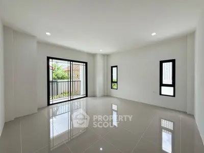 Spacious modern living room with large windows and balcony access, featuring sleek tile flooring and abundant natural light.
