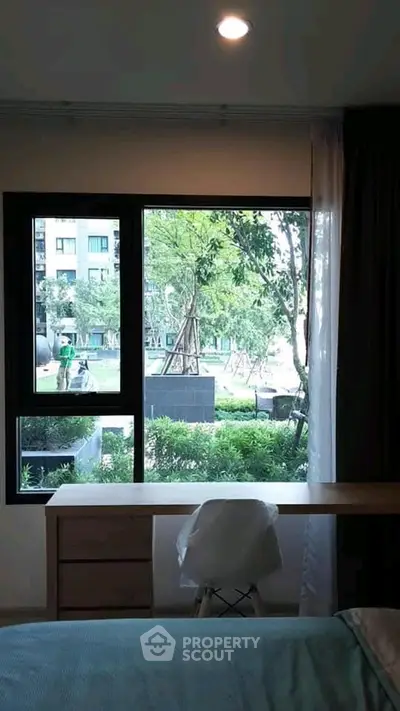 Cozy bedroom with garden view through large window, featuring a desk and chair for a serene workspace.