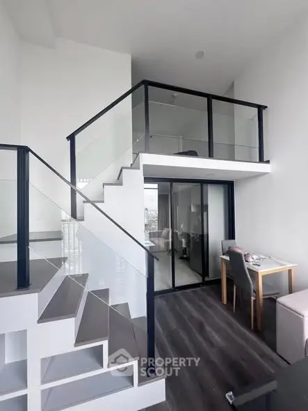 Modern loft apartment with sleek staircase and glass railing, featuring a cozy dining area and high ceilings.