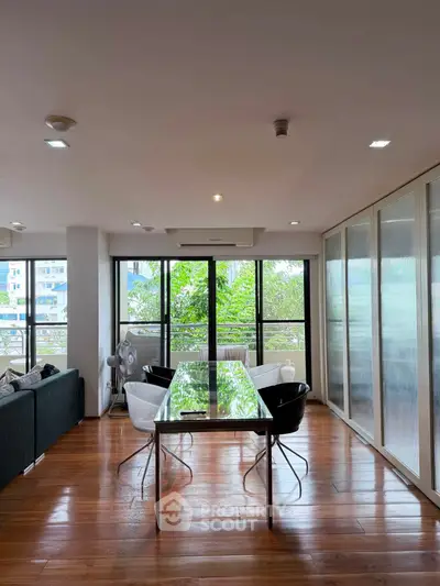 Spacious modern living room with large windows and elegant dining area, featuring hardwood floors and natural light.