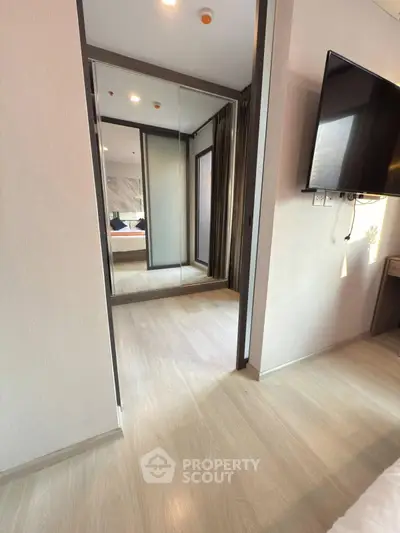 Modern bedroom with mirrored closet and wall-mounted TV in stylish apartment.