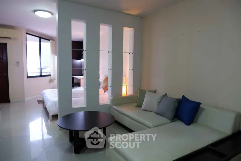 Modern living room with sectional sofa and view into cozy bedroom