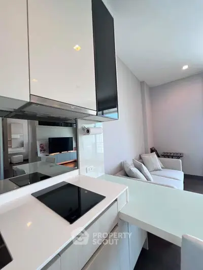 Modern kitchen with sleek induction cooktop and cozy living area in open-plan apartment.