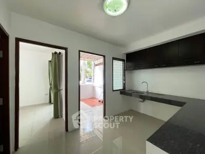 Modern kitchen with sleek countertops and open layout, adjacent to a bright room with large windows.