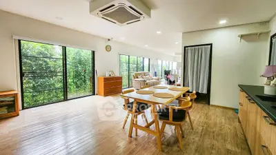 Spacious open-plan living room with dining area and large windows overlooking greenery.