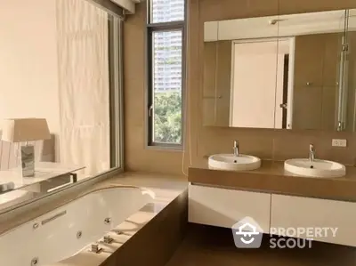 Luxurious bathroom with a large jacuzzi tub and dual vanity sinks, bathed in natural light from a floor-to-ceiling window.