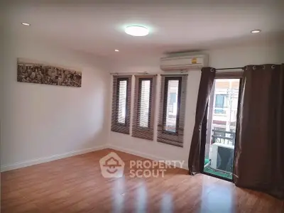 Spacious empty room with wooden flooring and large windows, perfect for customization.