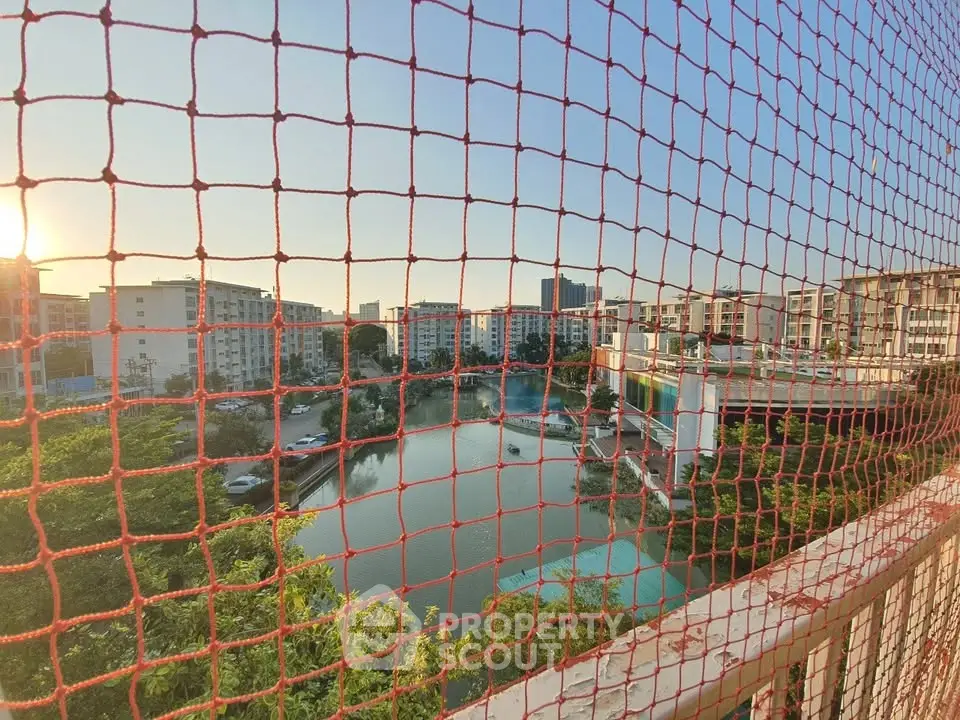 Scenic view of residential complex with pond and greenery, captured through safety netting.