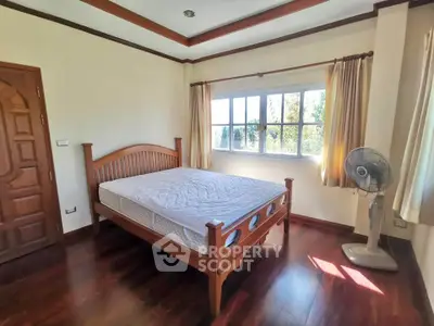Spacious bedroom with wooden flooring and large window offering natural light.