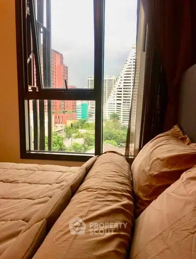 Cozy bedroom with city view through large window, featuring comfortable bedding and urban skyline.