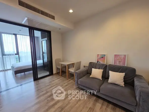 Modern living room with cozy sofa and dining area, adjacent to a bright bedroom with large windows.