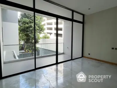 Spacious living room with floor-to-ceiling windows offering ample natural light and a view of the serene outdoor balcony area.