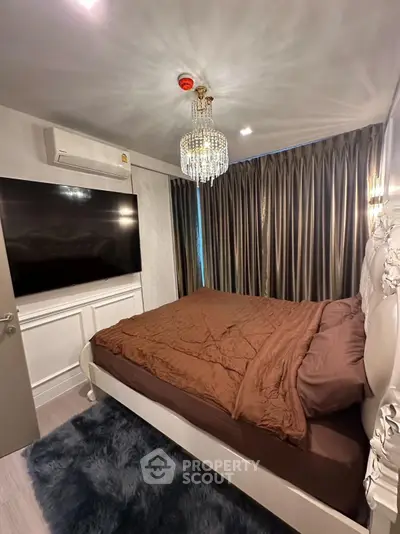 Luxurious bedroom with elegant chandelier and large TV, featuring plush bedding and modern decor.