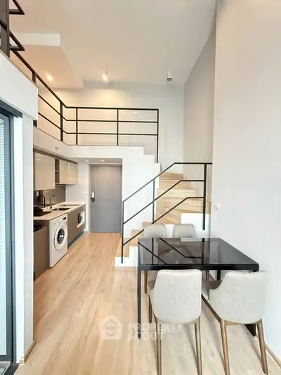 Modern duplex apartment with sleek staircase and open kitchen layout, featuring a washing machine and dining area.
