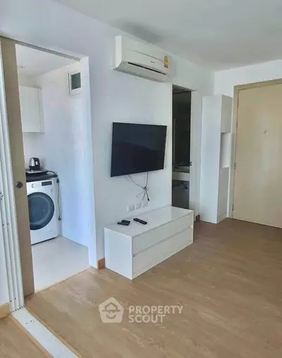Modern living room with wall-mounted TV and adjacent laundry area in a stylish apartment.