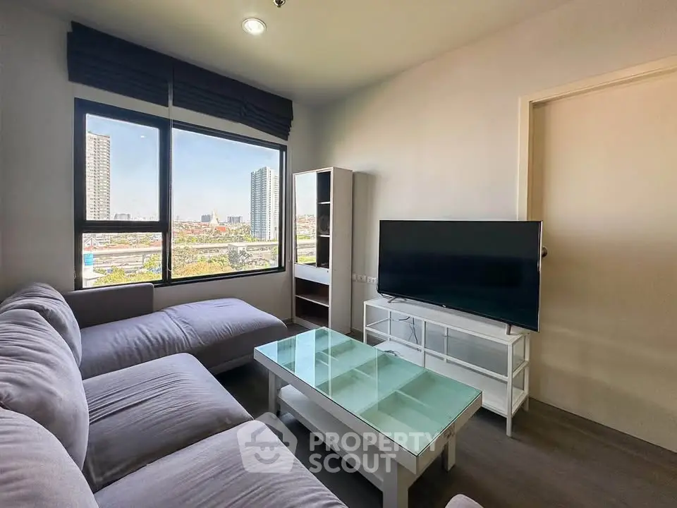 Modern living room with large window and city view, featuring a cozy sectional sofa and flat-screen TV.