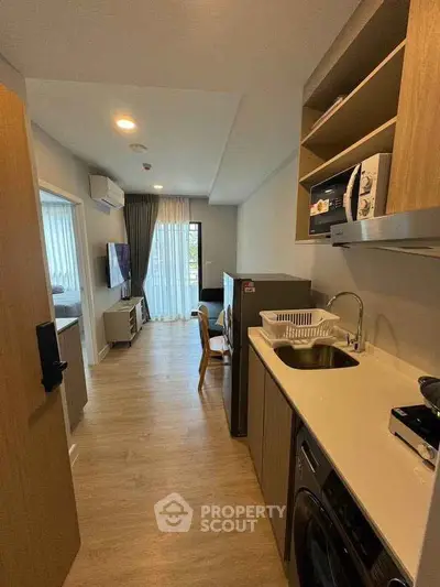 Modern apartment interior with open kitchen and living area, featuring sleek appliances and wooden flooring.
