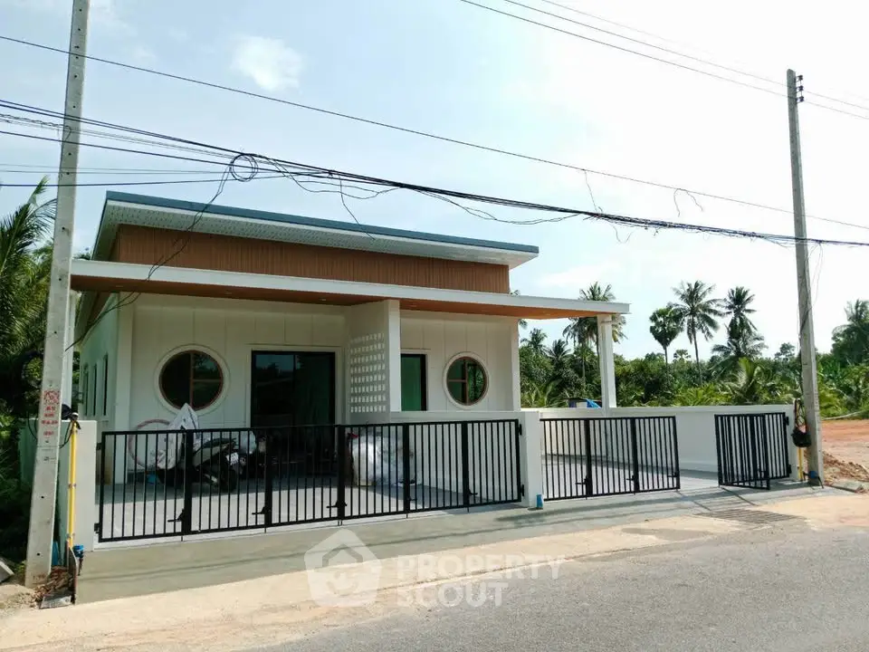 Modern single-story house with unique circular windows and gated driveway in tropical setting.